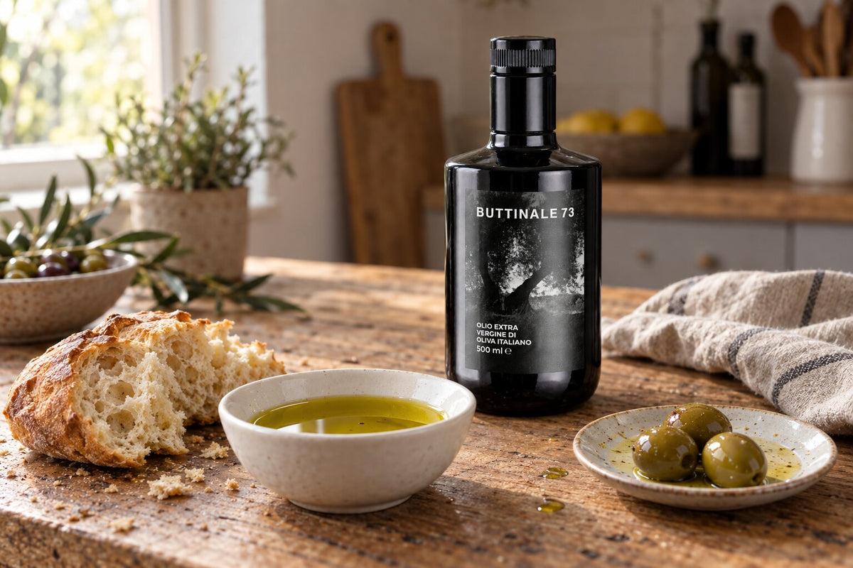 Schale mit frischem Olivenöl, Brot und Oliven auf einem Holztisch, dahinter eine Flasche BUTTINALE73 Manufaktur